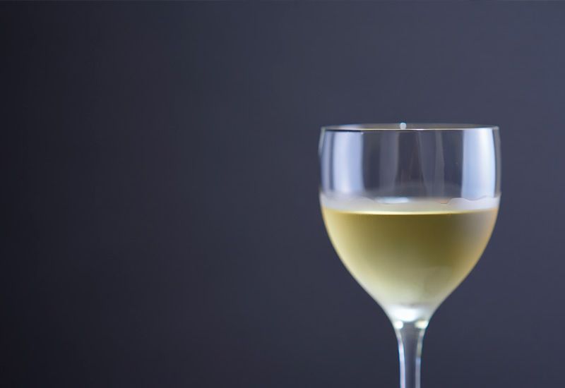 Бокал белого вина с золотистым оттенком стоит на тёмно-сером фоне